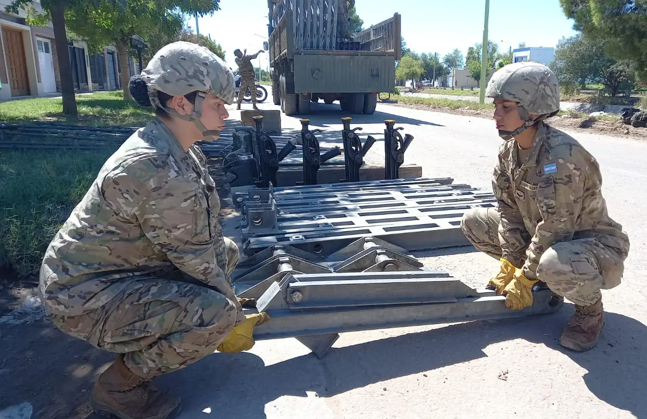Dos mujeres del Ejército Argentino levantando una parte del puente desde el piso